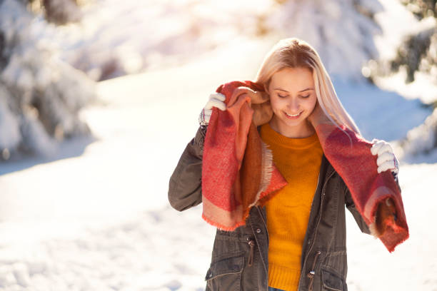 Blonde, young woman is putting on her warm scarf.