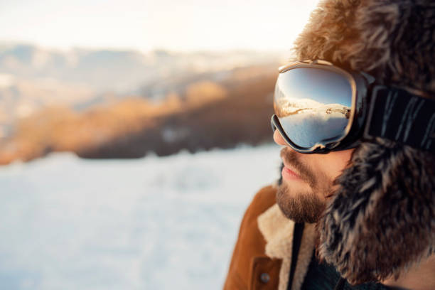 Side view of a young man with fur hat and ski googles.