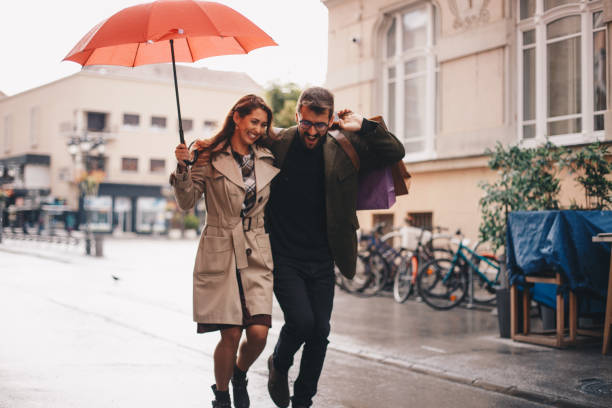 istock Young couple under umbrella smiling, running down the street 1279879103