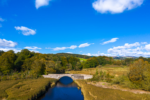 The view from a drone of an old stone bridge crossing a small river that flows into an estuary in Dumfries and Galloway, south west Scotland.