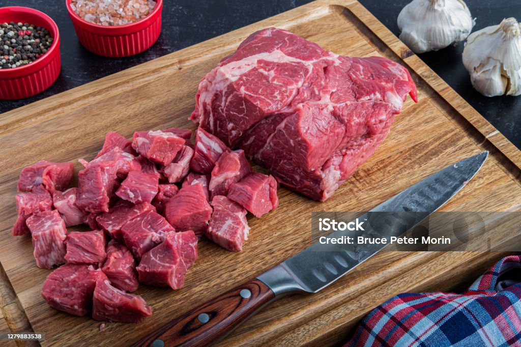 Boneless Beef Chuck Roast being cut into cubes for stew A boneless beef chuck roast being cubed for a stew on a cutting board with sea salt and peppercorns next to a carving knife Meat Stock Photo