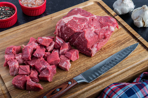 Boneless Beef Chuck Roast being cut into cubes for stew A boneless beef chuck roast being cubed for a stew on a cutting board with sea salt and peppercorns next to a carving knife roast beef photos stock pictures, royalty-free photos & images