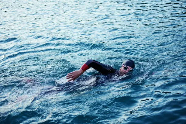 Photo of triathlon athlete swimming on lake in sunrise  wearing wetsuit