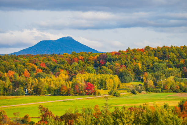 view of rural farm fields and forests  with Camels Hump Mountain in fall foliage season, in Vermont