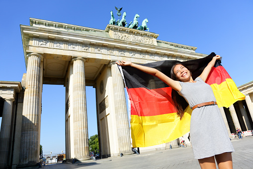 German flag - Woman happy at Berlin Brandenburger Tor cheering celebrating waving flag by Berlin Brandenburg Gate, Germany. Cheerful excited multiracial woman in Germany travel concept.