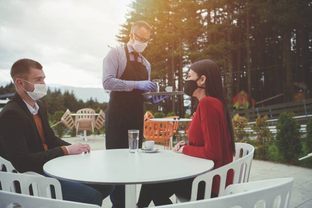 istock Waiter with protective medical mask and gloves serving guest 1279892461