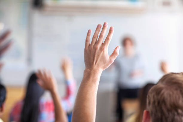 istock Male and female students raising hand in classroom 1279895910