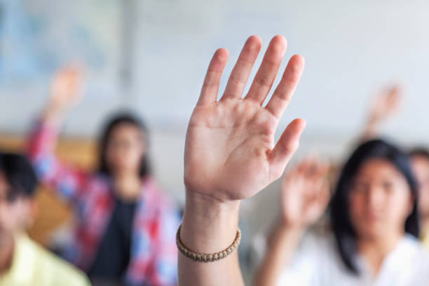 istock Teenager with hand raised sitting in classroom 1279895957