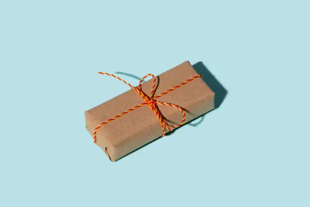 Birthday gift. Long-distance care package. Eco wrap. Holiday surprise. Vintage parcel. Rustic beige simple paper box with orange twine bow isolated on blue copy space background.
