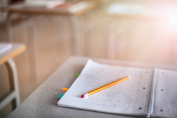 Close-up of pencil over book on desk at high school. School supplies arranged in illuminated education building. View of handwritten notes in empty classroom.