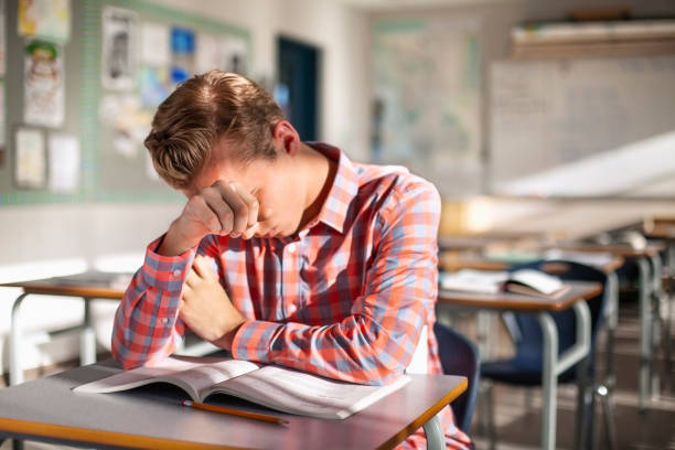 estudiante masculino estresado sentado con libro en el escritorio - sleeping high school desk education fotografías e imágenes de stock