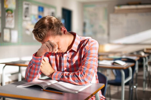 étudiant masculin stressé s’asseyant avec le livre au bureau - struggle photos et images de collection