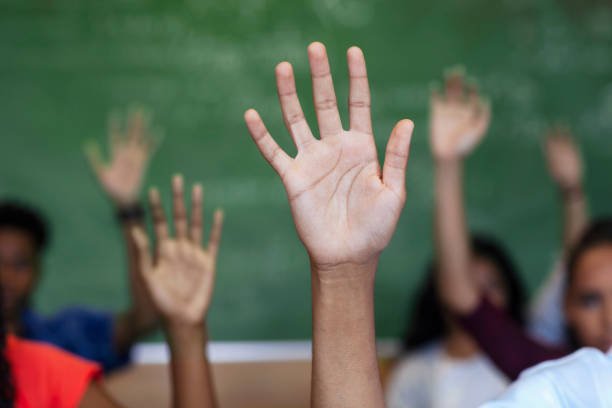 istock Diverse multi-cultural teenagers with hands raised sitting in classroom 1279901513