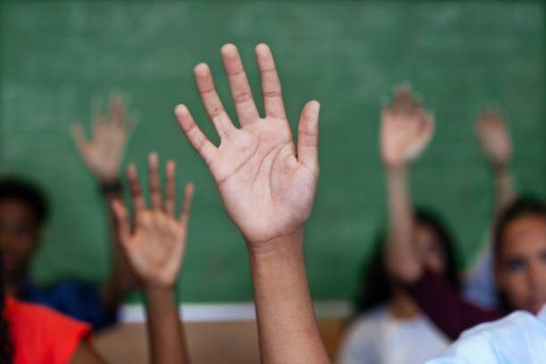 istock Diverse multi-cultural teenagers with hands raised sitting in classroom 1279901613