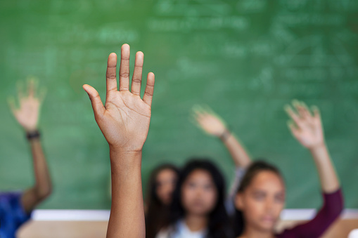 Cropped image of students with raised hands asking in lecture hall. High school teenagers are learning at education building. They are in classroom.