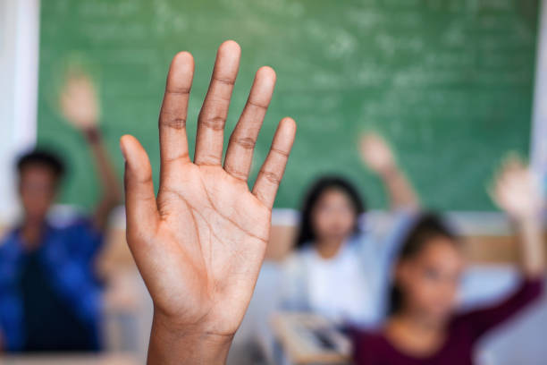 istock Diverse multi-cultural teenagers with hands raised sitting in classroom 1279902230