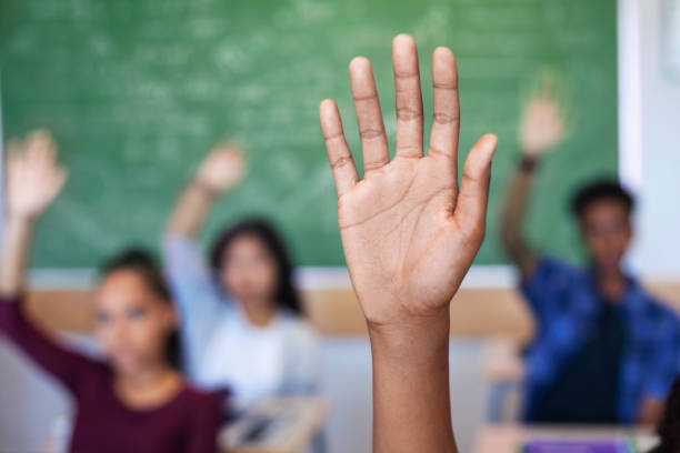 istock Diverse multi-cultural teenagers with hands raised sitting in classroom 1279902263
