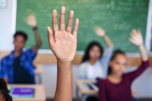 istock Diverse multi-cultural teenagers with hands raised sitting in classroom 1279902292