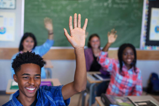 istock Smiling diverse multi-cultural students raising hands in classroom 1279902327