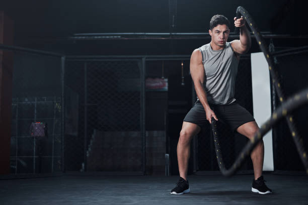 Be as strong as you were born to be Shot of a young man working out with battle ropes at a gym HIIT Workout stock pictures, royalty-free photos & images