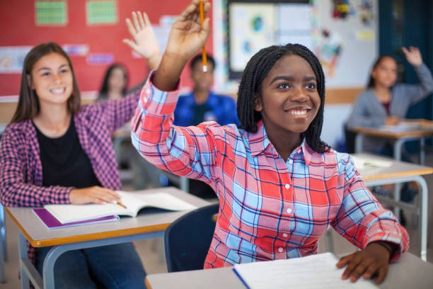 istock Smiling diverse multi-cultural students raising hands in classroom 1279902727