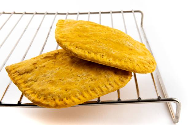two West Indies patties on a wire rack isolated on white the meat and vegetarian patty are staple food items in the Caribbean, Jamaica and Trinidad Jamaican Beef Patty stock pictures, royalty-free photos & images