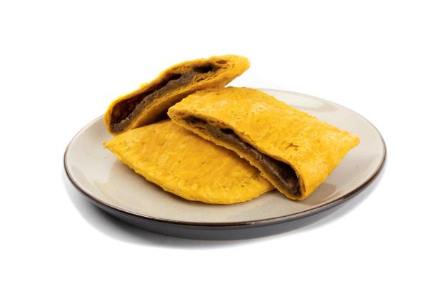 two Caribbean beef patties on a plate with one cut open isolated on white
