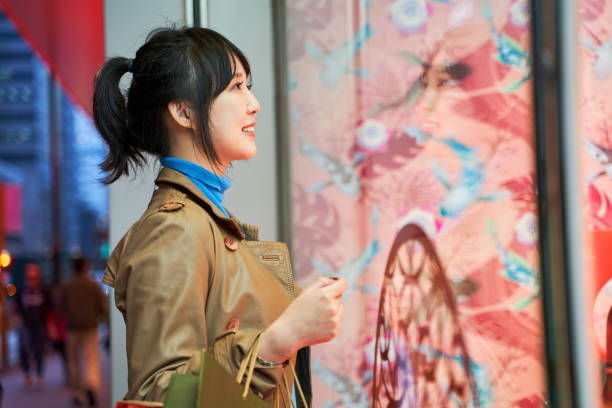 beautiful happy young asian woman shopper looking into shop window in modern city