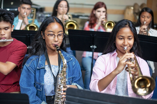 Confident Asian teenage girls playing brass instruments in classroom. Students are practicing music at high school. They are learning musical instruments.