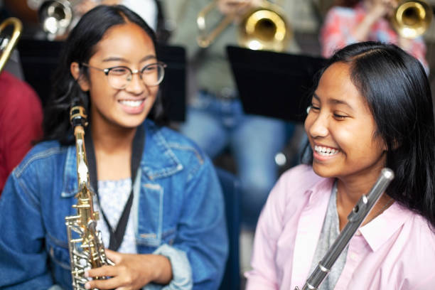 studentesse asiatiche di musica mista che parlano e ridono con strumenti in ottone in classe - band name immagine foto e immagini stock