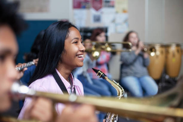 garota asiática de etnia mista alegre com saxofone na classe orquestra de banda - music class - fotografias e filmes do acervo