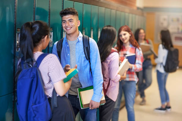 Smiling teenage students talking at high school Smiling teenage students talking while standing in illuminated corridor; boy is Middle Eastern ethnicity. Female and male friends are by lockers in education building. They are at high school. teen romance stock pictures, royalty-free photos & images