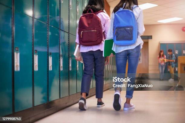 Female Classmate Friends With Backpacks Walking By Lockers In School Stock Photo - Download Image Now