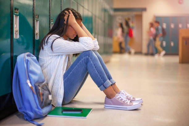 Frustrated Asian teenage young woman female student with head in hands in hallway in school Frustrated teenage female student sitting with head in hands. Side view of high school girl in illuminated corridor. She is against metallic lockers. child sadness stock pictures, royalty-free photos & images