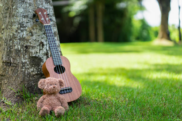 istock Ukulele guitar with bear doll under the tree on green grass field with sunlight 1279910833