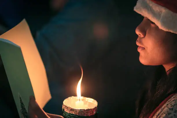 A children singer hands holding candle and book with singing carol song on celebration of christmas day background