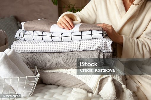 istock Beautiful woman in winter thick warm robe is sitting and neatly folding bed linens and bath towels 1279912899