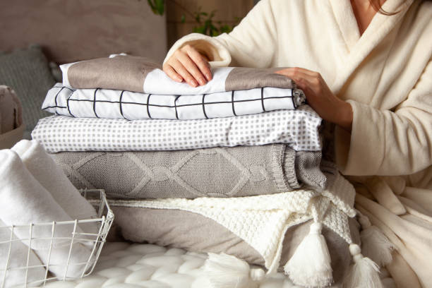 Beautiful woman in winter thick warm robe is sitting and neatly folding bed linens and bath towels Beautiful woman in winter thick warm robe is sitting and neatly folding bed linens and white bath towels. Organizing and sorting clean laundry. Organic and natural cotton textile. Manufacture. bedding stock pictures, royalty-free photos & images