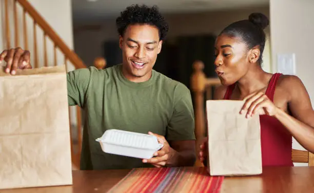 african american couple sitting at table looking at food delivery at home