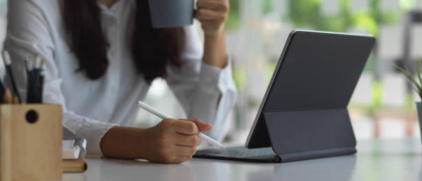 istock Female hand holding stylus pen and drinking coffee while using tablet 1279915891