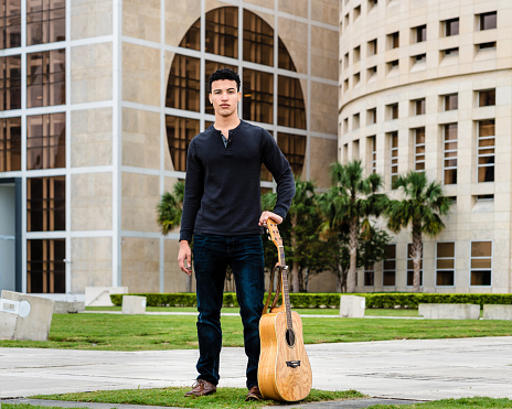 Young musician posing with his guitar in the city park; art and performance college student