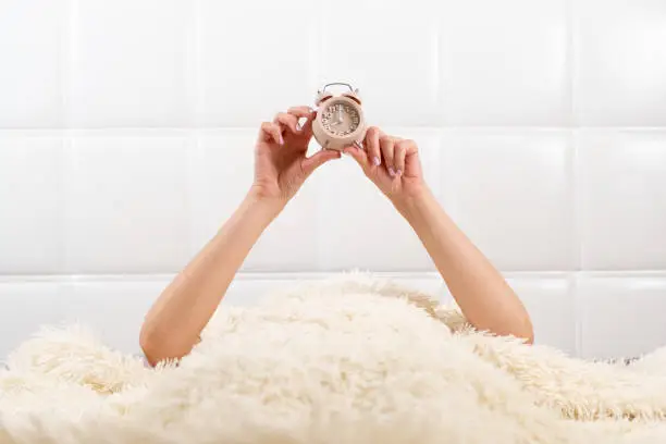 Photo of Female hands hold alarm clock in bed, time concept, wonderful start of a new day, good morning. copy space