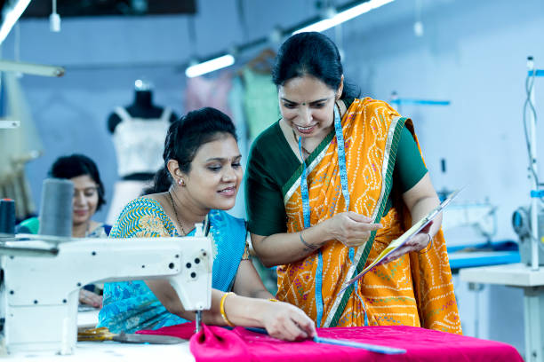 ispettore che guida l'operaia tessile che cuce indumenti sulla linea di produzione - manual worker sewing women tailor foto e immagini stock