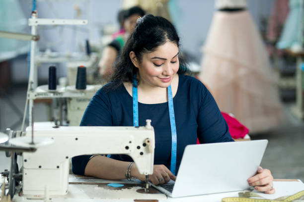 woman using laptop at textile factory - sewing tailor sewing machine women imagens e fotografias de stock