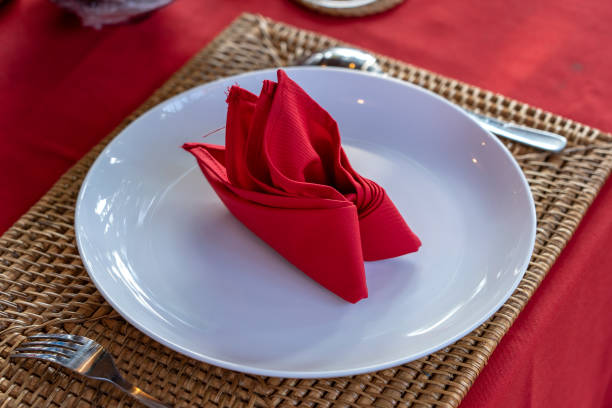istock Elegant table setting with fork, spoon, white plate and red napkin in restaurant . Nice dining table set with arranged silverware and napkins 1279930264