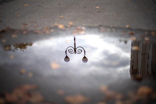 Reflection of a pole with a lantern and a gray sky in an autumn puddle. Focus on the center