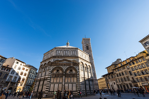 Firenze, Italy, January 3, 2013: Baptistery of San Giovanni (St. John the Baptist) and Florence Cathedral, Santa Maria del Fiore, with the Bell Tower of Giotto (Campanile). UNESCO world heritage site, Tuscany, Italy, Europe. A group of tourists and locals stroll around the famous square.