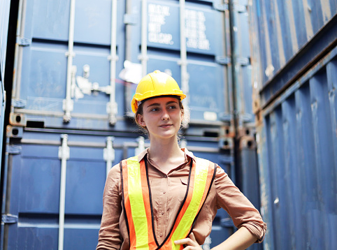Young Woman Engineers standing in the shipping yard tracking the cargo inventory and checking container box for safety.