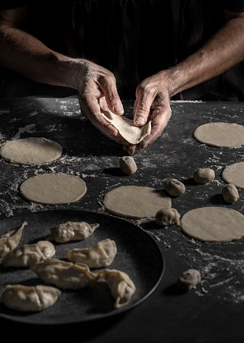 Gyoza Dumplings preparation man hands with balls dough circles and finished Gyozas on a kitchen