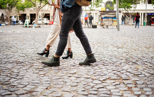 Close-up of two unrecognizable friends walking together through a cobblestone square in the city